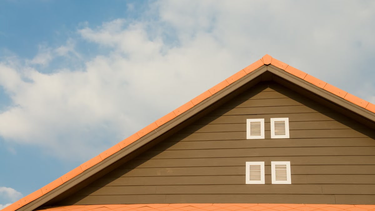 Modern house facade featuring orange roof and shuttered windows against a bright blue sky.